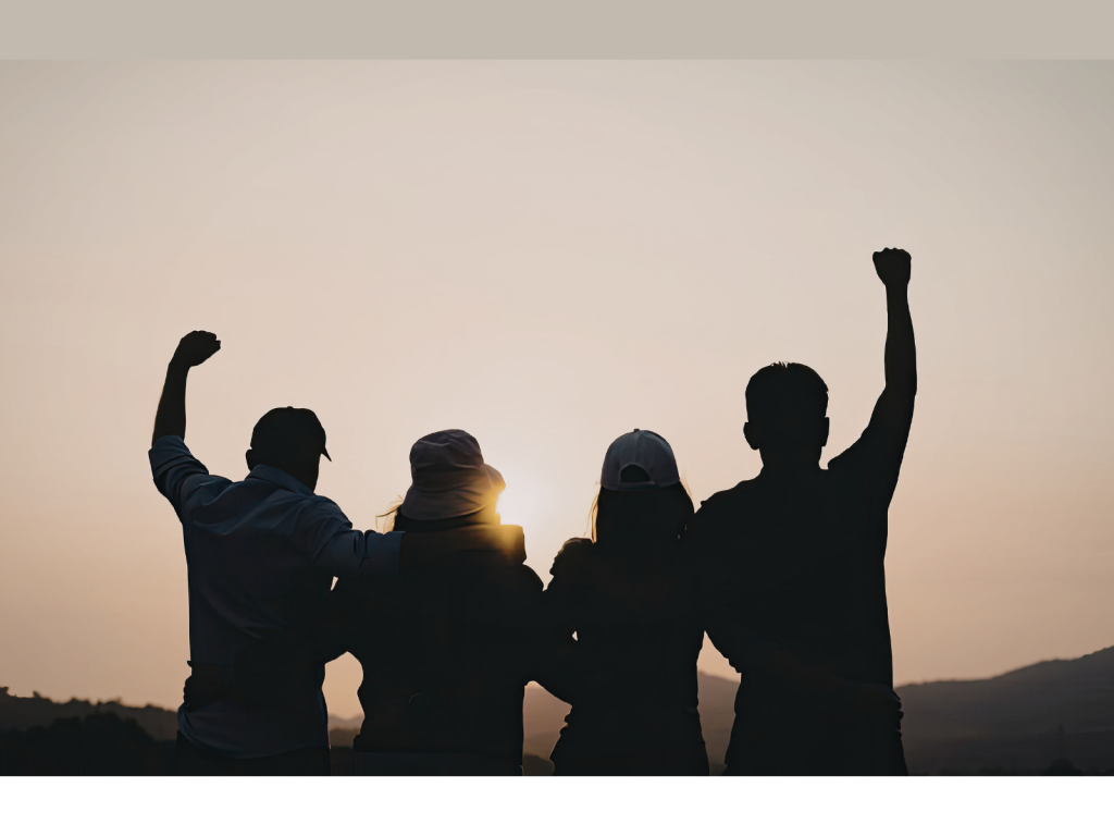 Silhouette of four people standing together against a sunset with raised fists, symbolizing a successful partnership and collective impact.